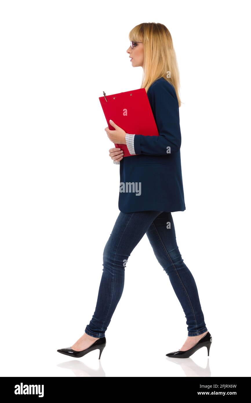 Jeune femme d'affaires en costume bleu et talons hauts marche avec presse-papiers. Vue latérale. Prise de vue en studio pleine longueur isolée sur fond blanc. Banque D'Images