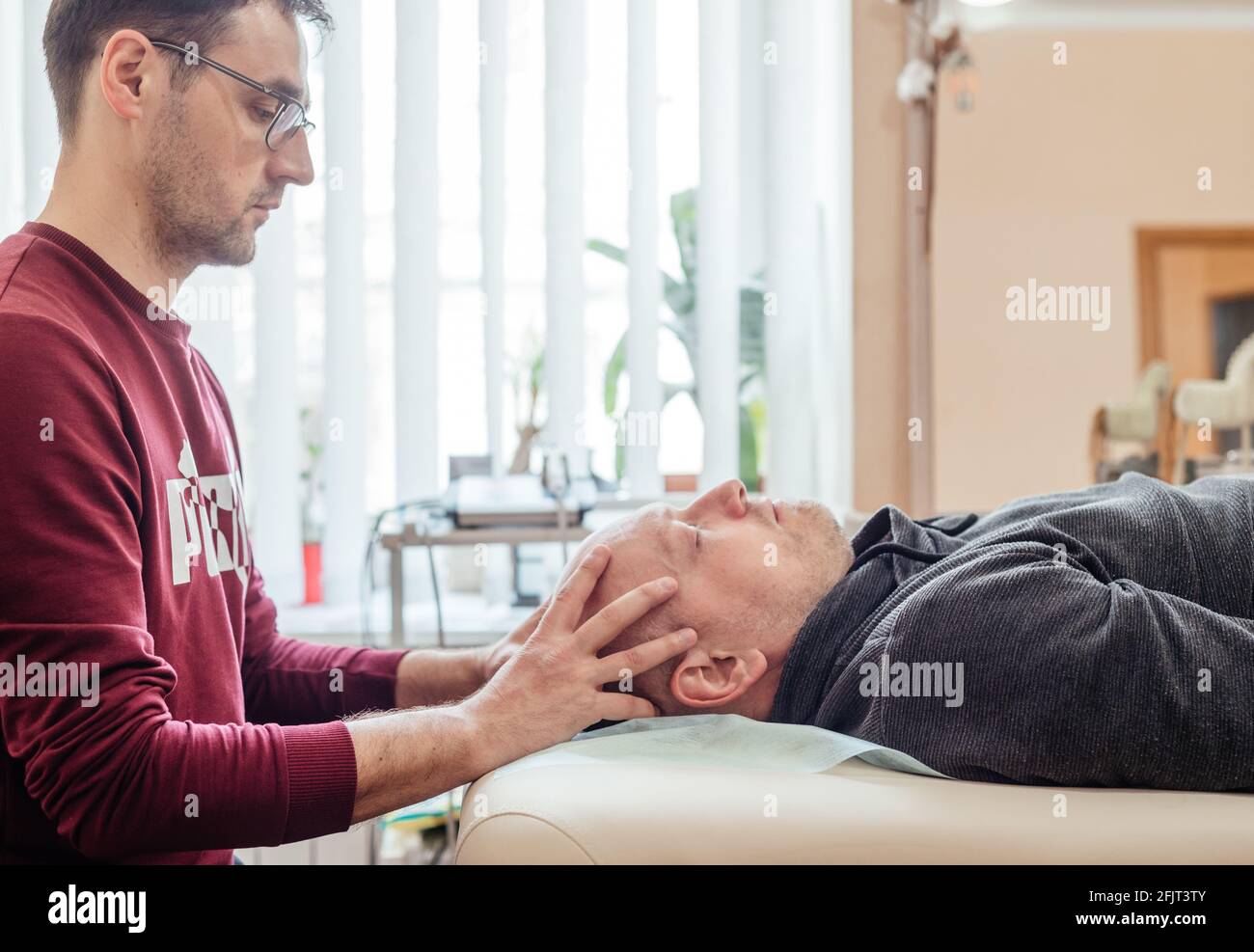 Patient masculin recevant un traitement sacral crânien, allongé sur la table de massage dans la clinique ostéopathique CST, ostéopathie et thérapie manuelle Banque D'Images