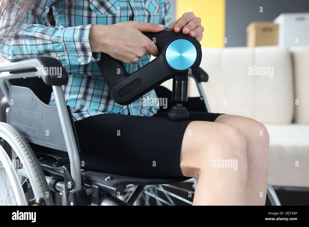 Femme handicapée en fauteuil roulant effectuant un massage des jambes avec un masseur à percussion gros plan Banque D'Images