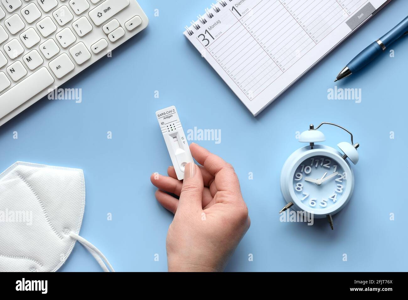 Planificateur de semaine, chnelltest, test rapide de corona en langue allemande. Plat avec calendrier, clavier, réveil. Main tenant l'antigène express corona Banque D'Images