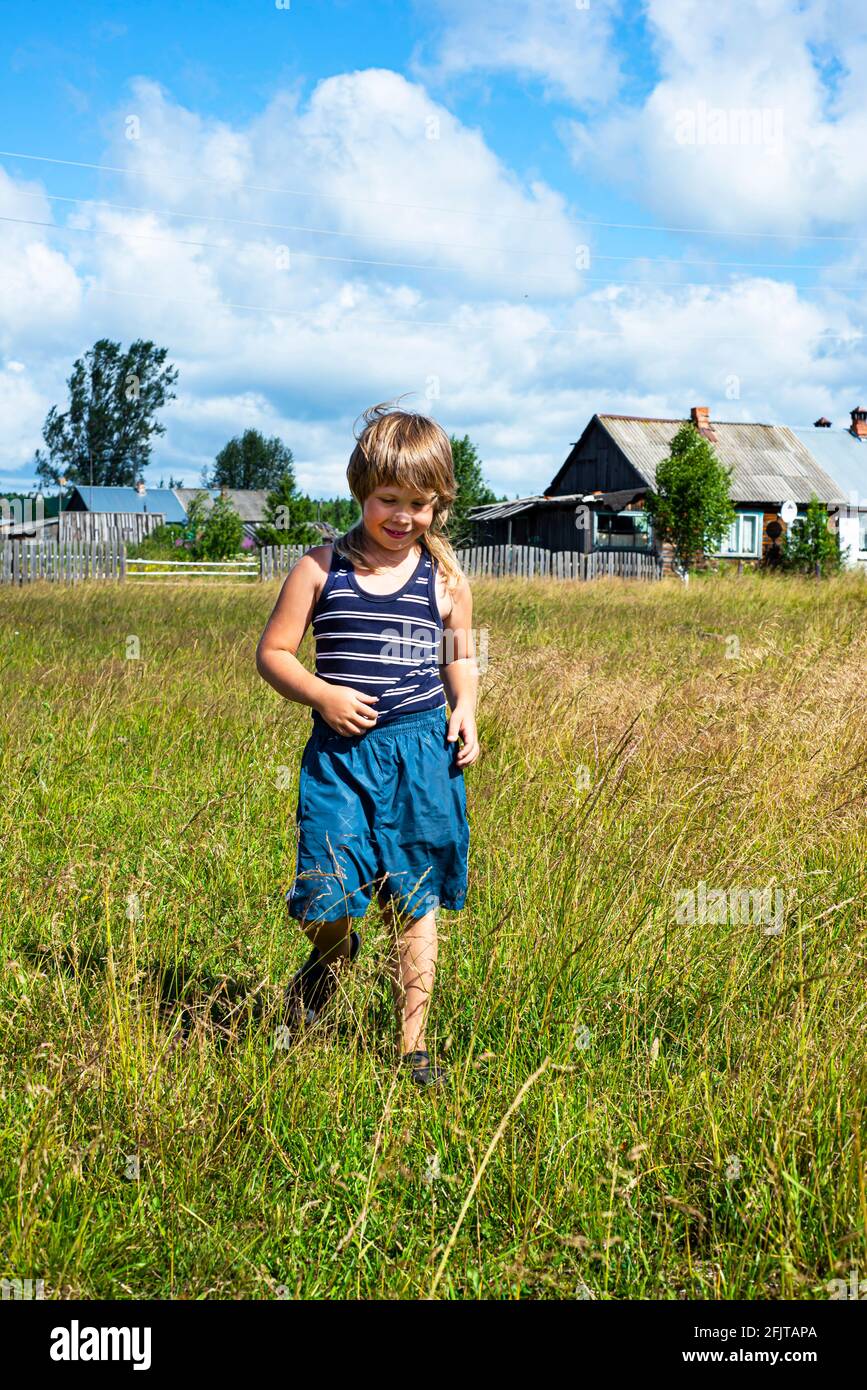 Un garçon en short et un t-shirt rayé se promène dans la prairie. Mode de vie rural. Émotions positives. Trafic. Joie et bonne humeur. Banque D'Images