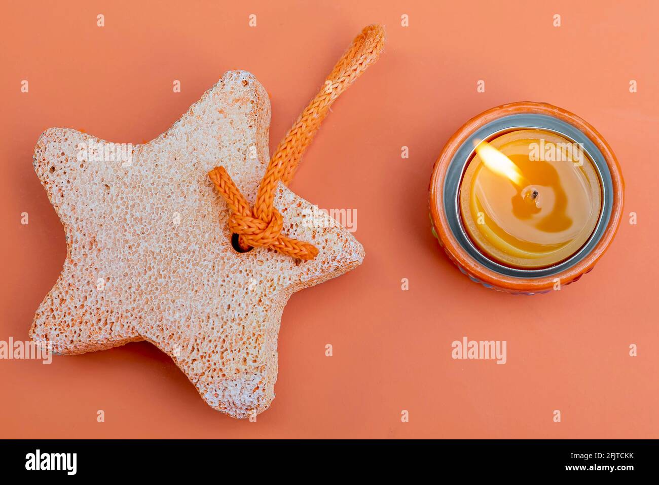 Une pierre ponce orange avec une bougie allumée à côté sur fond orange Banque D'Images
