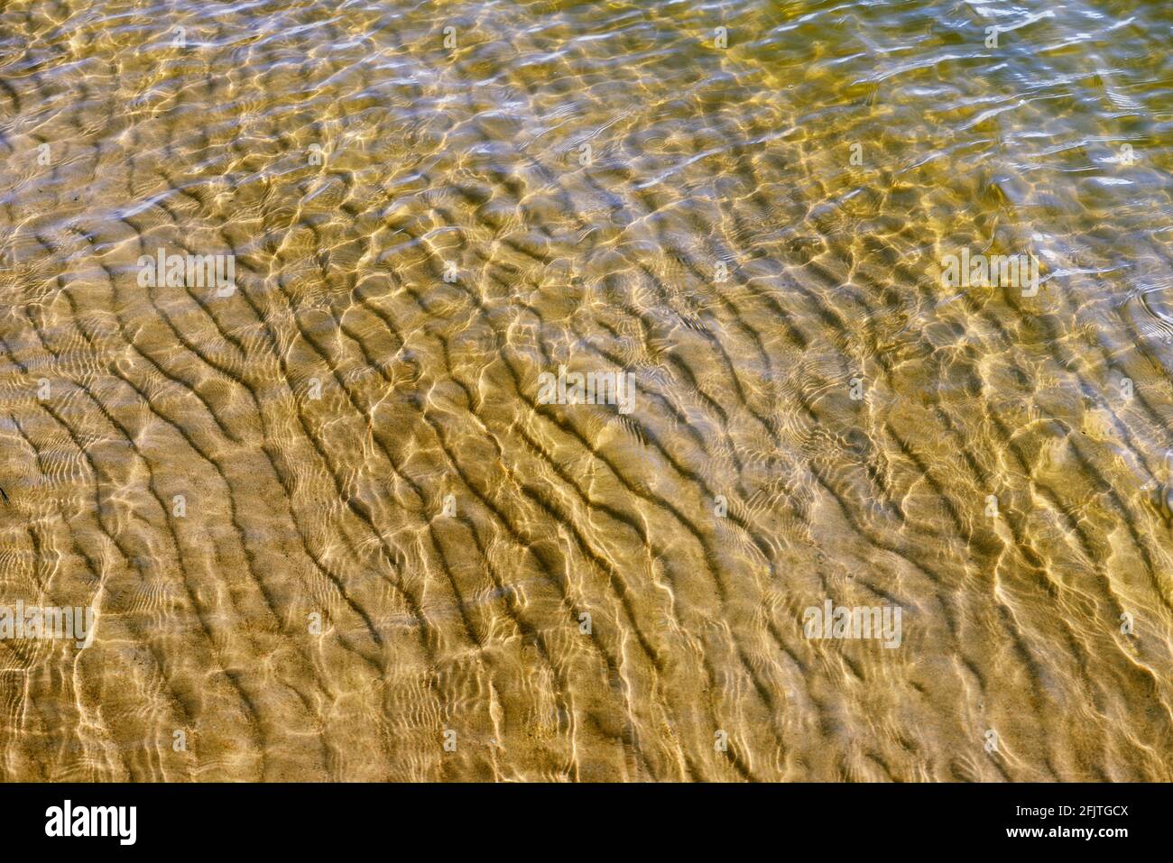 la surface de l'eau est percée par les rayons du soleil, le fond sablonneux est visible à travers l'eau Banque D'Images