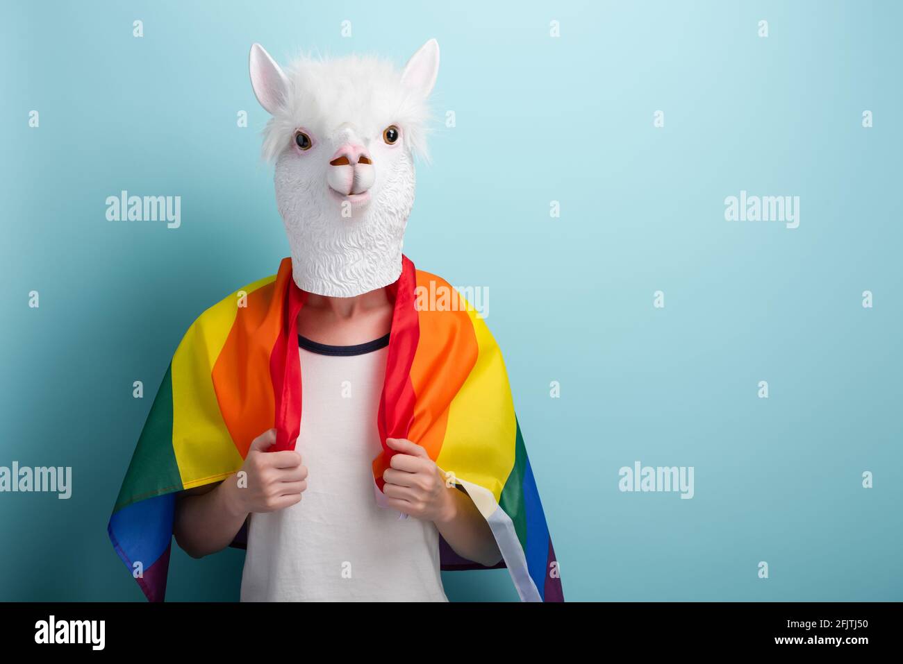 La jeune femme en masque de lion porte fièrement le drapeau de fierté lgbt arc-en-ciel enveloppé autour des épaules, isolé sur fond bleu avec l'espace de copie. Banque D'Images