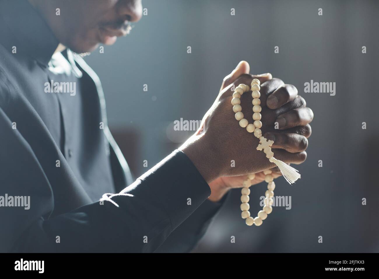 Gros plan de l'homme africain tenant des perles dans ses mains et prier dans l'église Banque D'Images