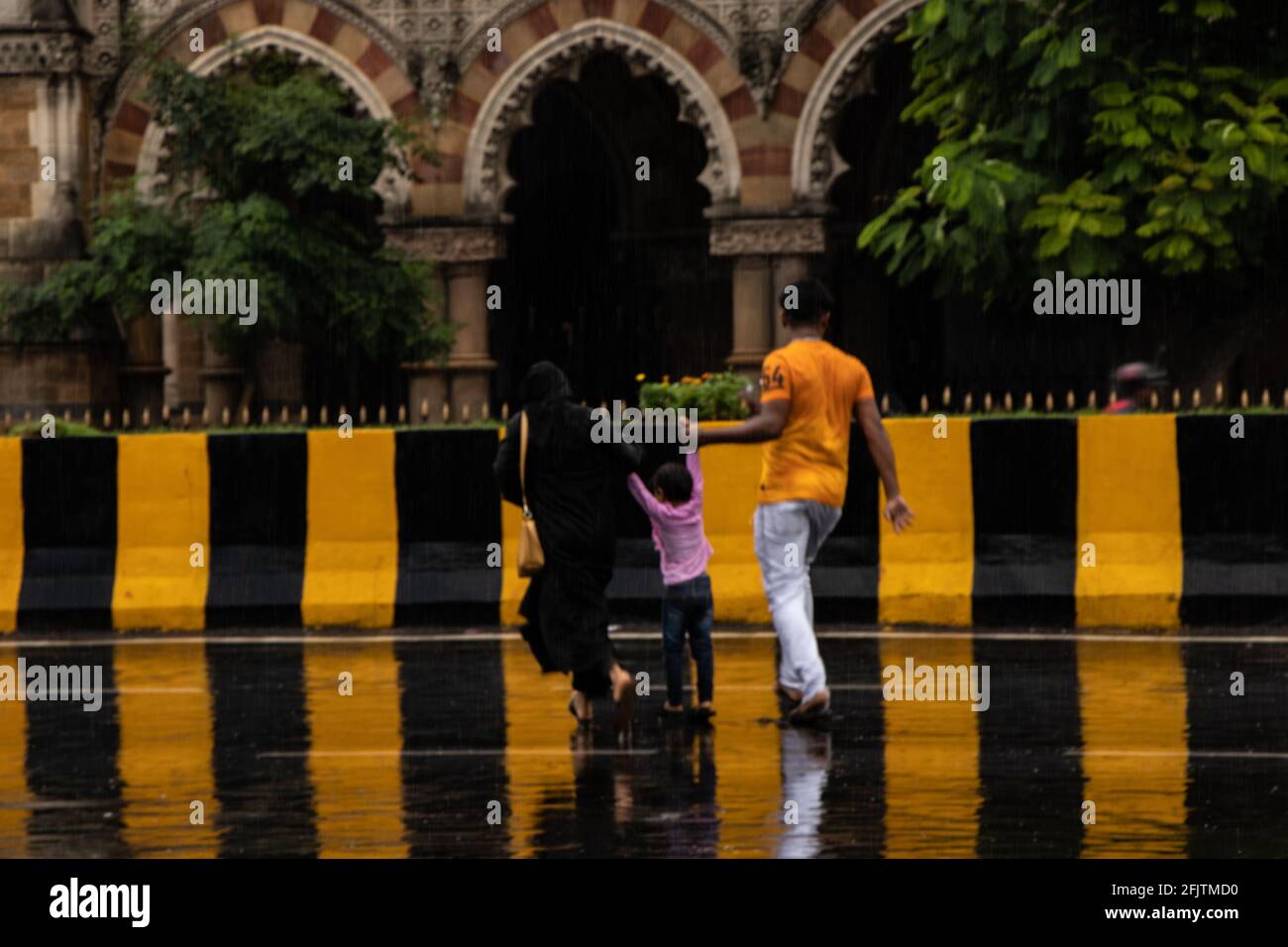 Famille traversant la rue sous la pluie avec une bande barrière de route qui réfléchit au sol Banque D'Images