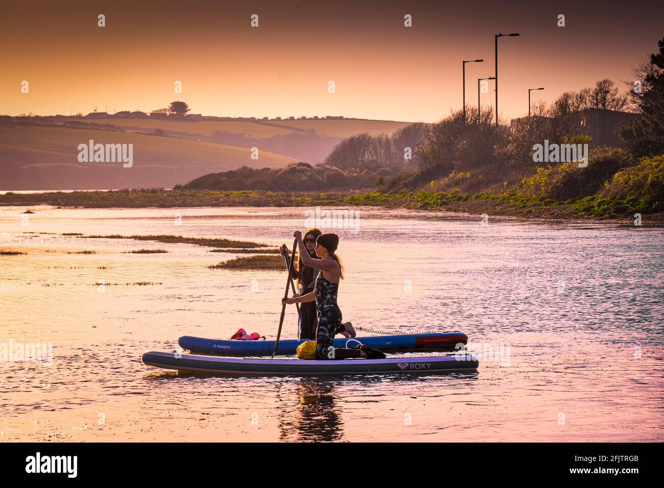 Feu d'or en soirée, deux planchistes femelles sur les paddleboards Stand Up paddle à marée haute sur la rivière Gannel à Newquay dans les Cornouailles. Banque D'Images