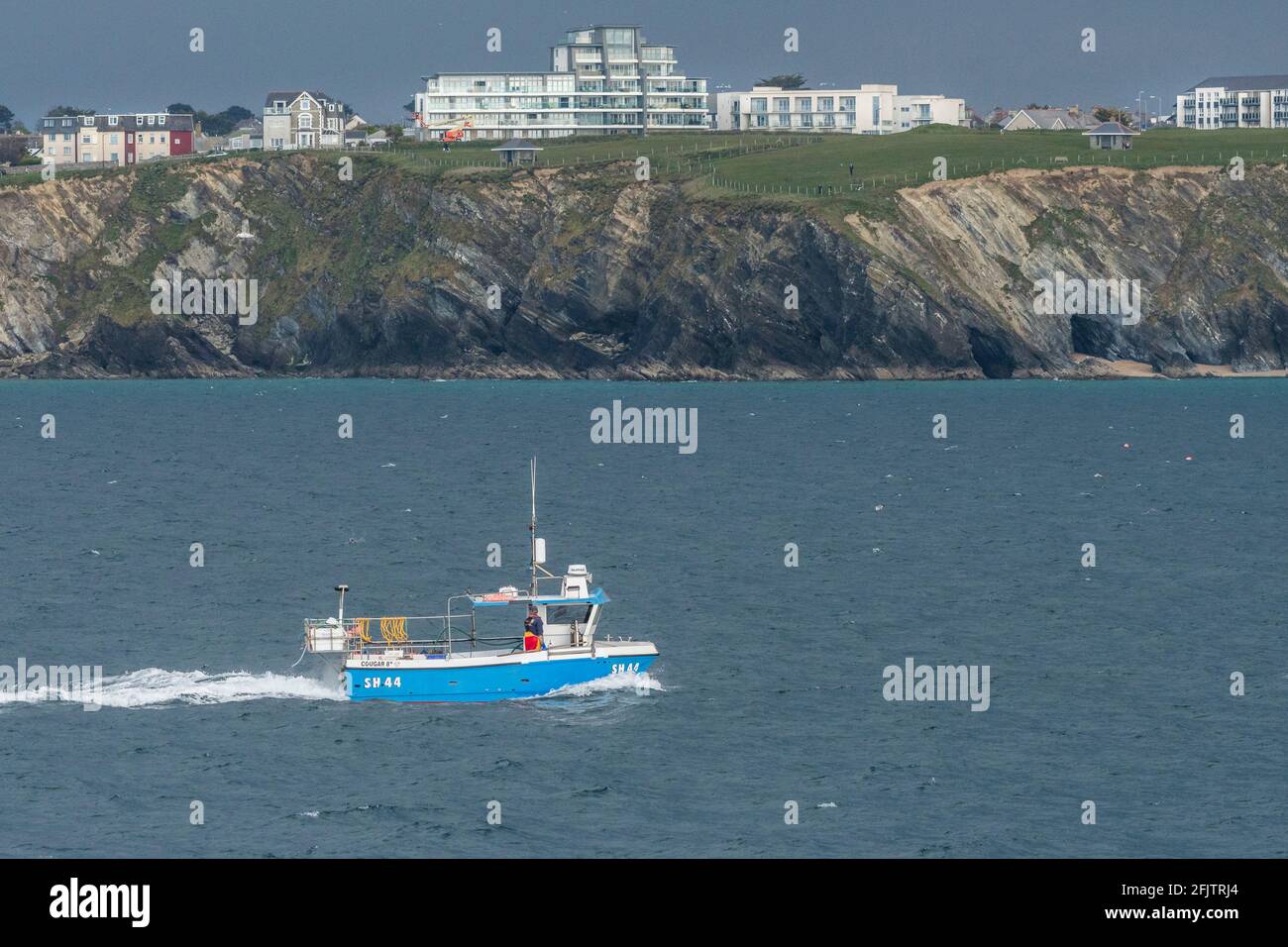 Le bateau de pêche Odyssey qui passe devant les champs de Barrowfields et surplombe la baie de Newquay sur la côte nord de Cornwall. Banque D'Images