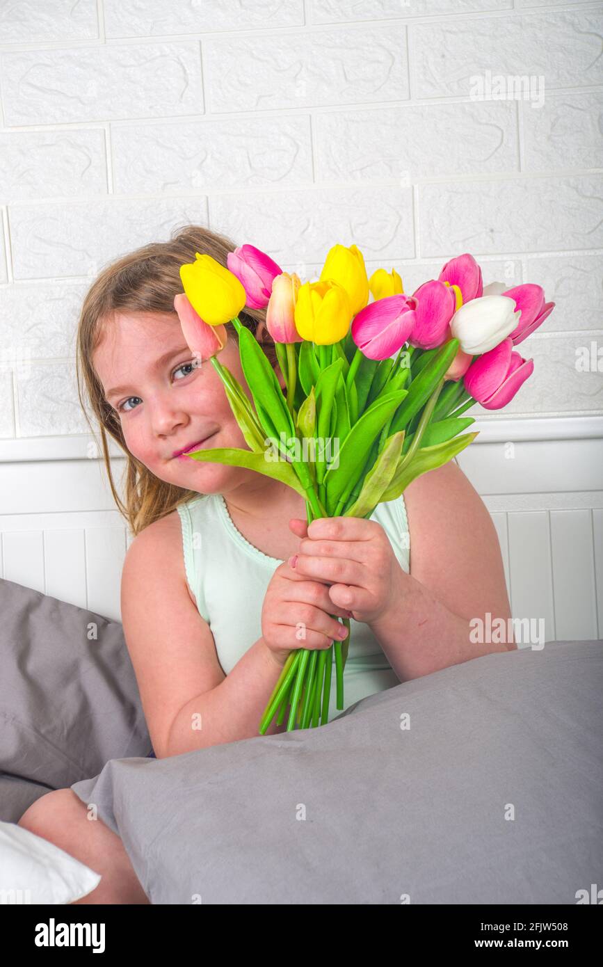 Fête des mères, fête des filles concept de style de vie. Enfant jeune fille blonde jeune fille avec un bouquet de fleurs de tulipe, carte de vœux faite à la main Banque D'Images