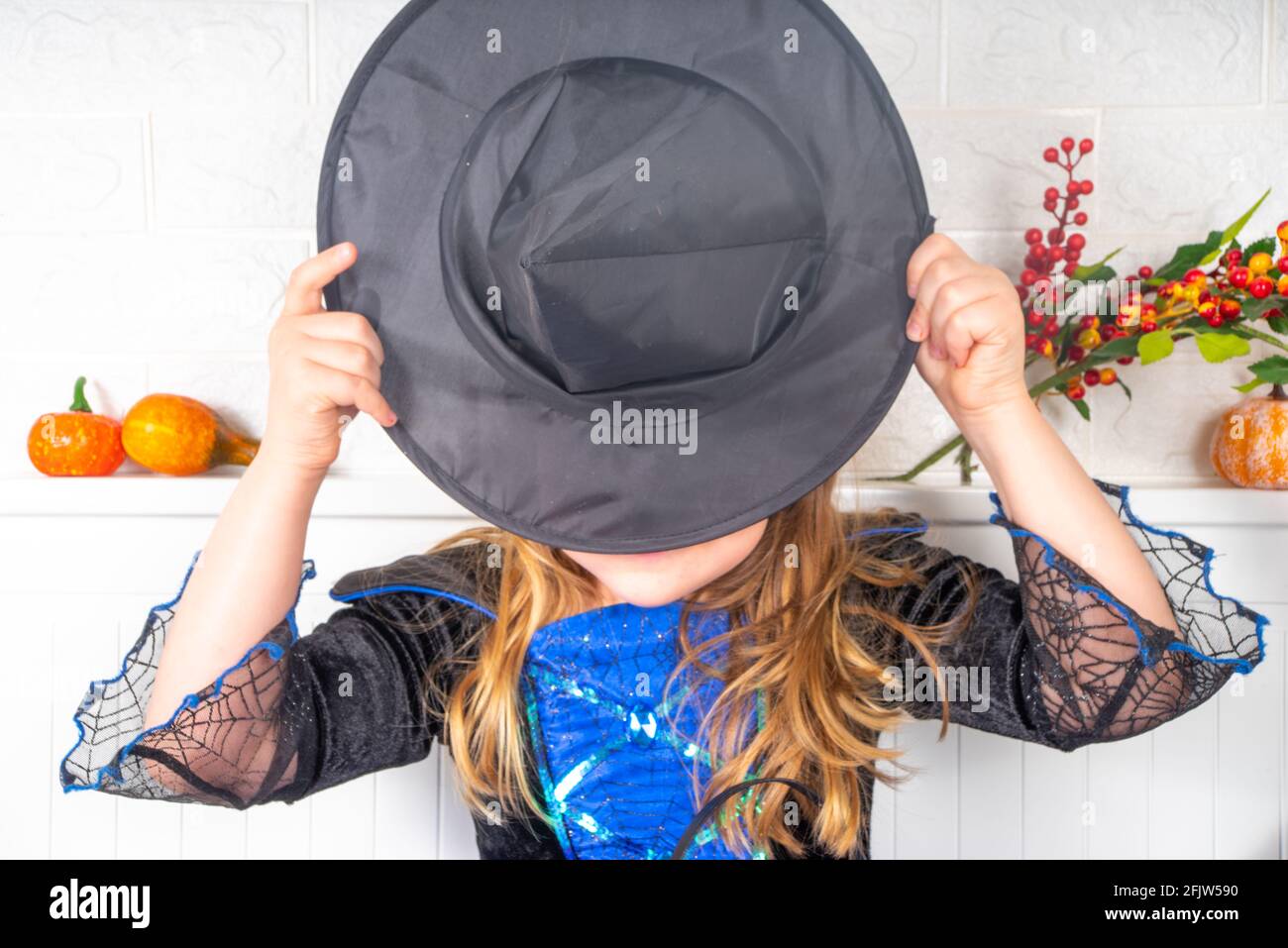 Vacances d'automne Halloween arrière-plan. Bonne fille caucasienne dans une robe et un chapeau de sorcière, avec des seaux de bonbons dans la maison ou un espace de copie de jardin d'enfants Banque D'Images