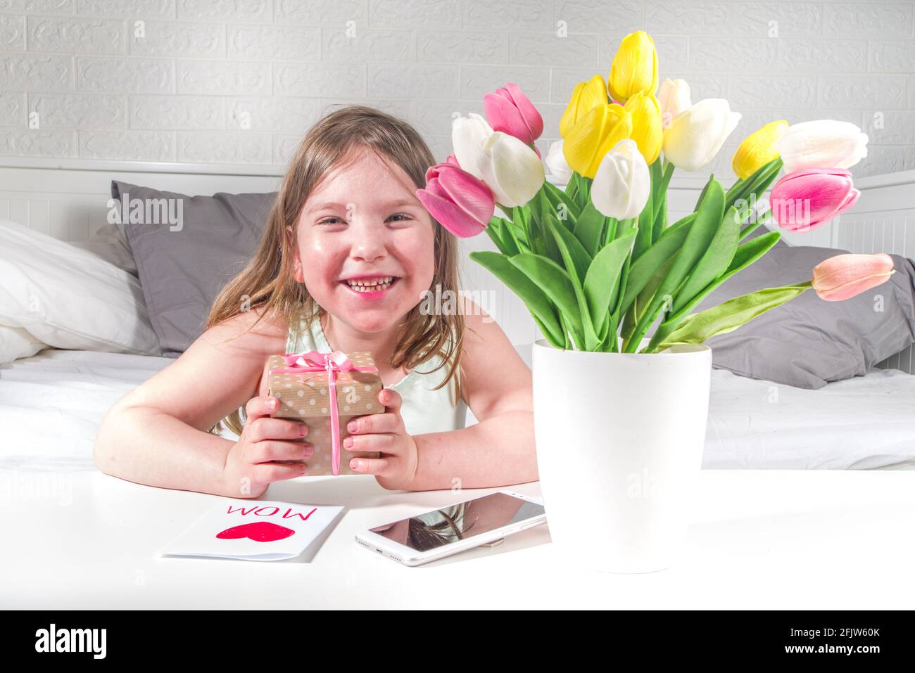 Fête des mères, fête des filles concept de style de vie. Enfant jeune fille blonde jeune fille avec un bouquet de fleurs de tulipe, carte de vœux faite à la main Banque D'Images