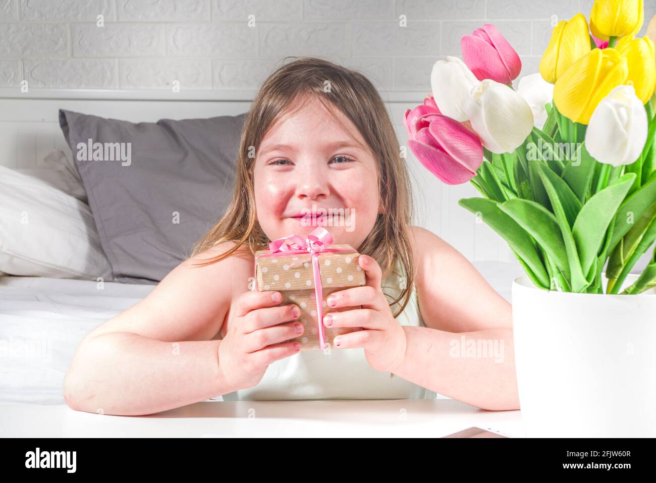 Fête des mères, fête des filles concept de style de vie. Enfant jeune fille blonde jeune fille avec un bouquet de fleurs de tulipe, carte de vœux faite à la main Banque D'Images