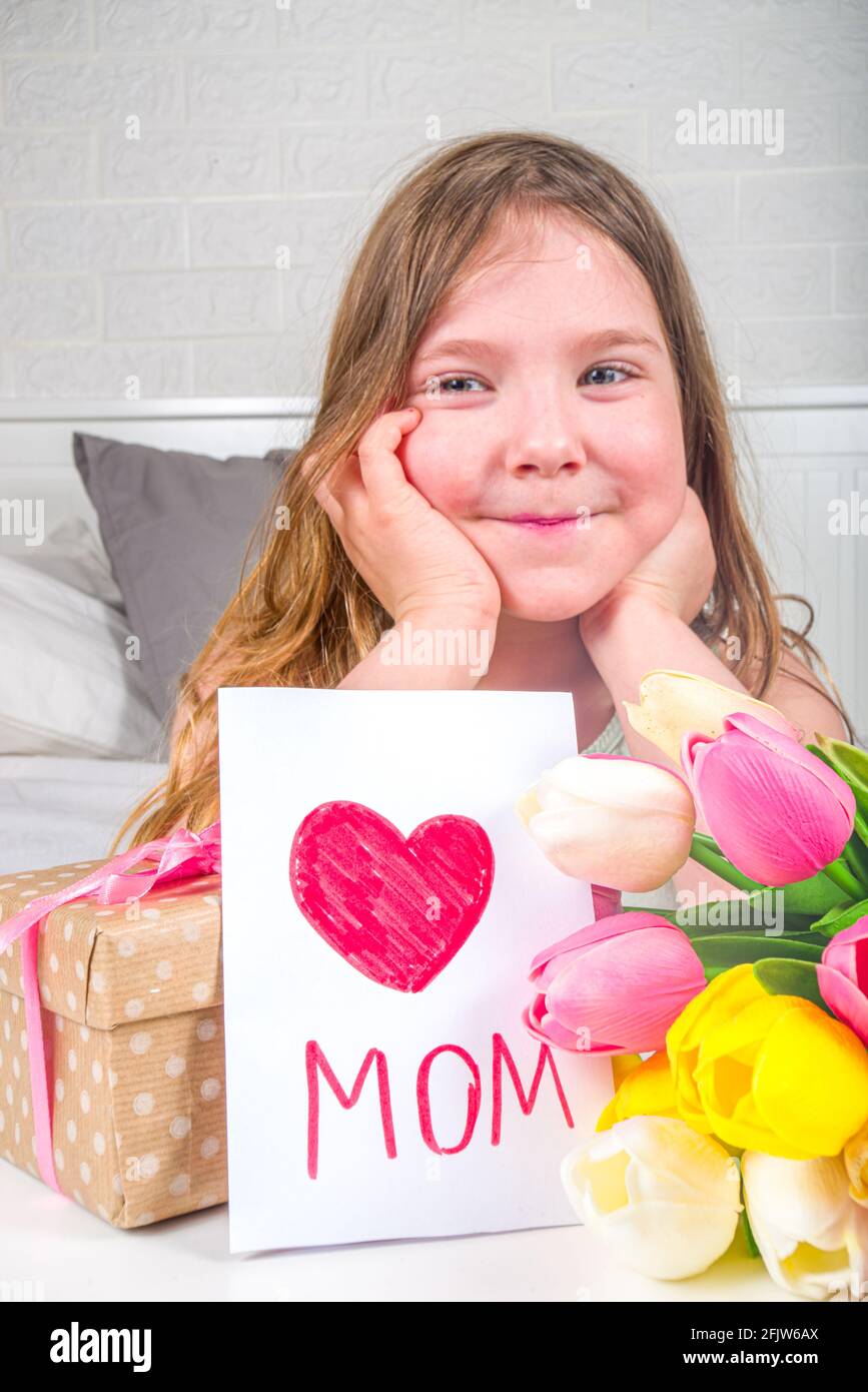 Fête des mères, fête des filles concept de style de vie. Enfant jeune fille blonde jeune fille avec un bouquet de fleurs de tulipe, carte de vœux faite à la main Banque D'Images