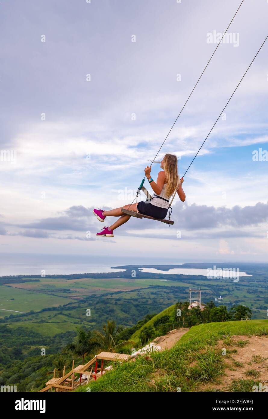 Une jeune fille, blonde, se balançant sur une balançoire sur une pente de montagne en été. Balancer haut dans les montagnes au-dessus de la vallée. République dominicaine. Réglage du soleil Banque D'Images