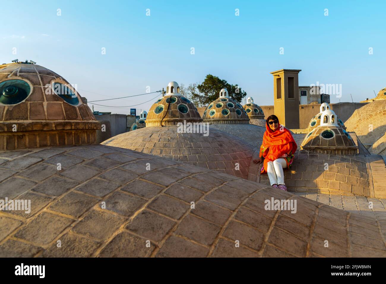 Dame avec foulard orange assis sur le toit avec plusieurs dômes de la salle de bain du Sultan Amir Ahmad ( ou Qasemi ) . Kashan, Iran. Banque D'Images