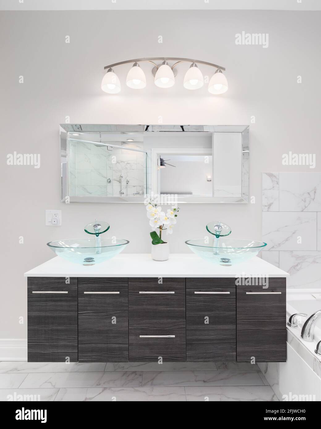 Une belle salle de bains meuble-lavabo en bois sombre avec comptoir en granit blanc, lavabos en cristal, grand miroir rectangulaire et carrelage en marbre. Banque D'Images