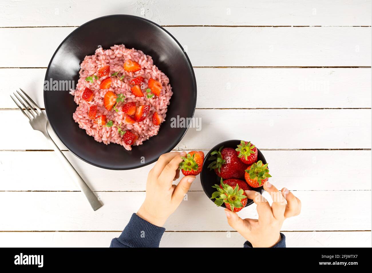 Risotto aux fruits à la fraise servi dans un plat noir sur une table en bois blanc. plat avec espace de copie. Cuisine gastronomique italienne. Mise au point sélective. Banque D'Images