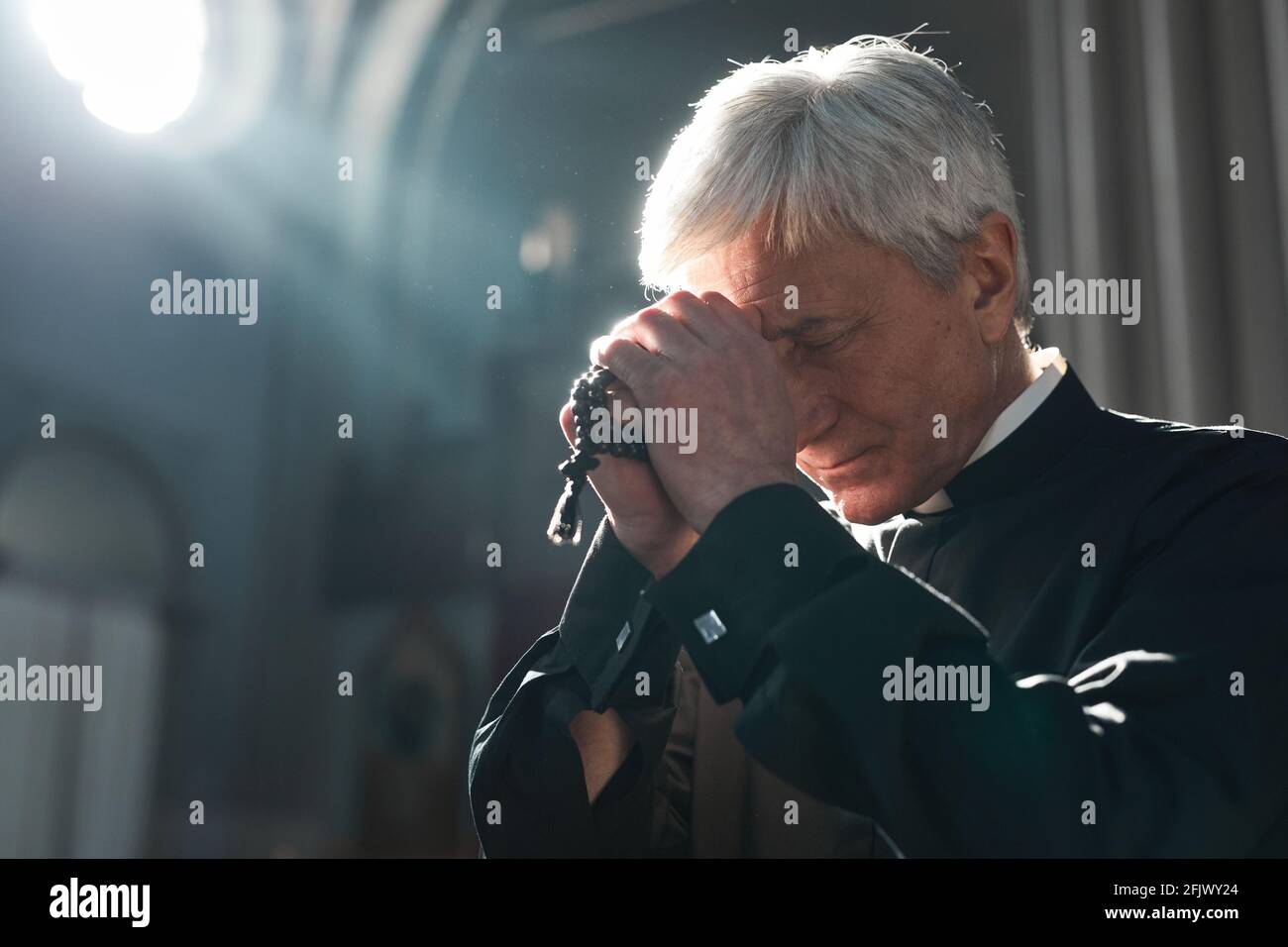 Prêtre principal tenant des perles rosaires priant tout en étant assis dans le église Banque D'Images