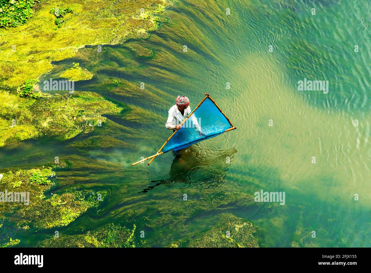 Un pêcheur pêche avec des filets faits à la main dans les algues d'une rivière sèche à la fin de l'hiver. Banque D'Images