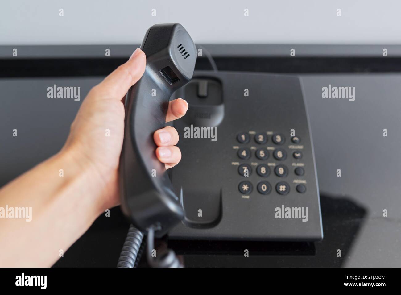 Téléphone dans une chambre d'hôtel, main avec un récepteur téléphonique surélevé de près Banque D'Images