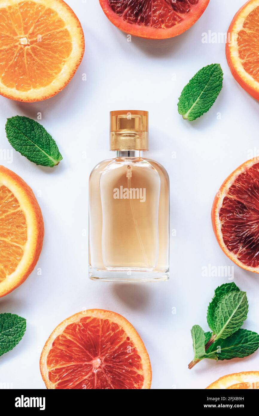 Bouteille de parfum et différentes tranches d'agrumes oranges rouges avec feuilles de menthe verte sur fond blanc. Concept de cosmétiques naturels de beauté biologique Banque D'Images