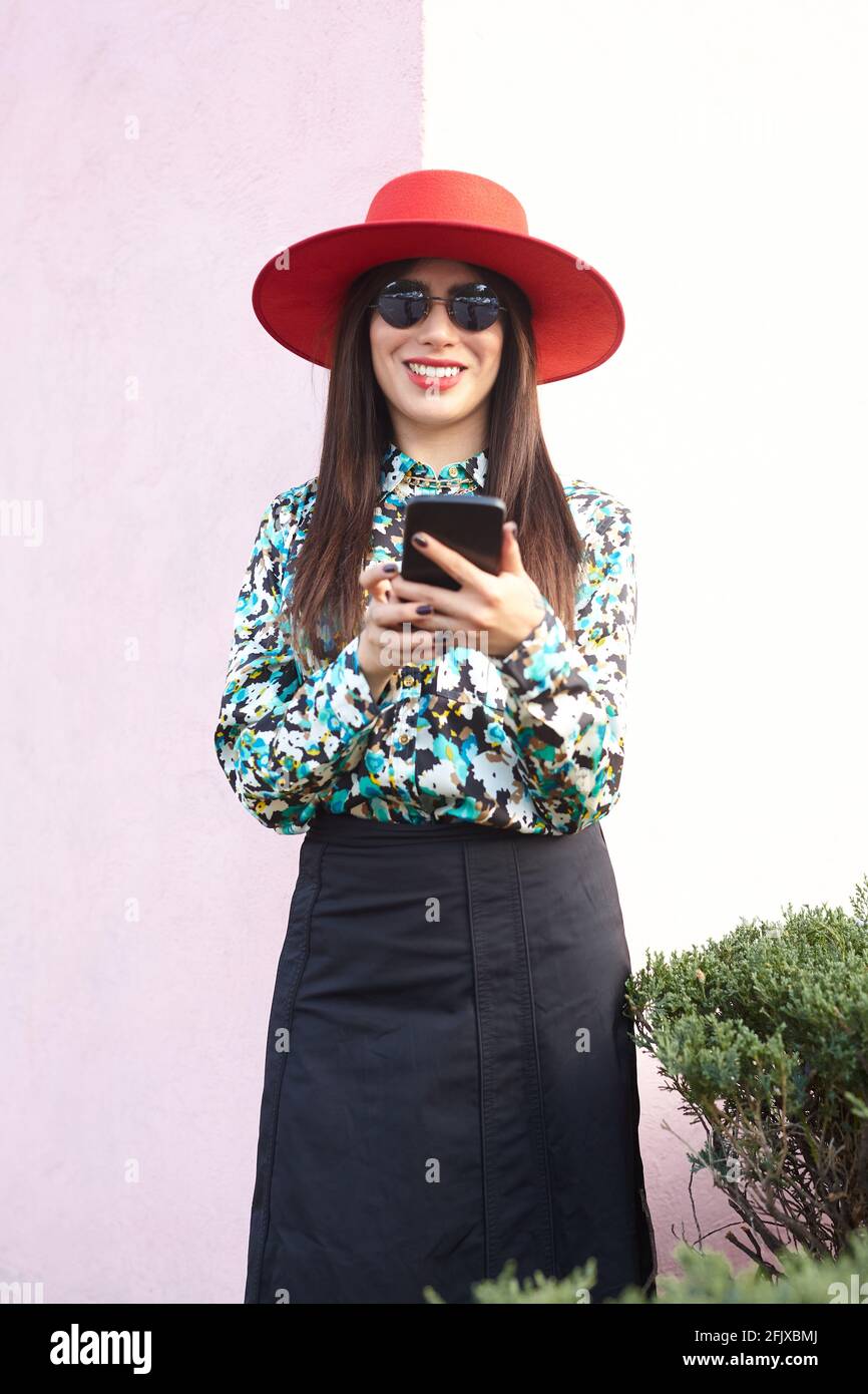 Portrait d'une jeune femme élégante utilisant son téléphone intelligent un mur rose Banque D'Images