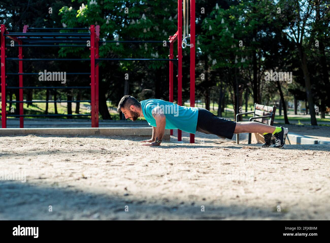 Garçon aux cheveux sombres avec une barbe qui pousse dans un parc. Arrière-plan des bars de fitness rouges. Banque D'Images