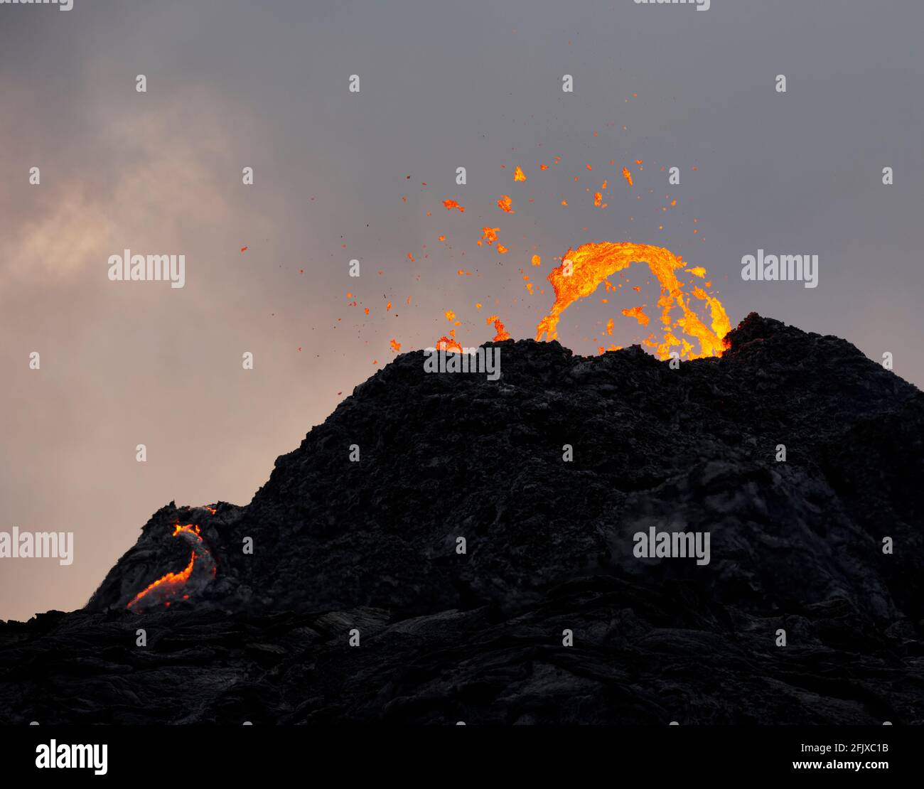 Lave d'orange sur carter de volcan en éruption au coucher du soleil Banque D'Images