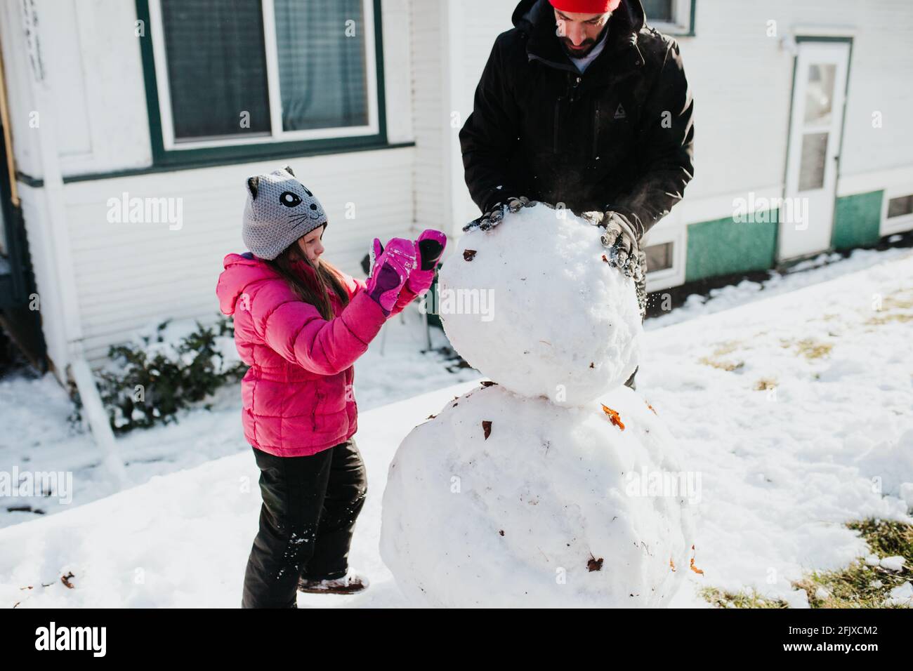 Père et fille construisent bonhomme de neige à l'extérieur de la maison Banque D'Images