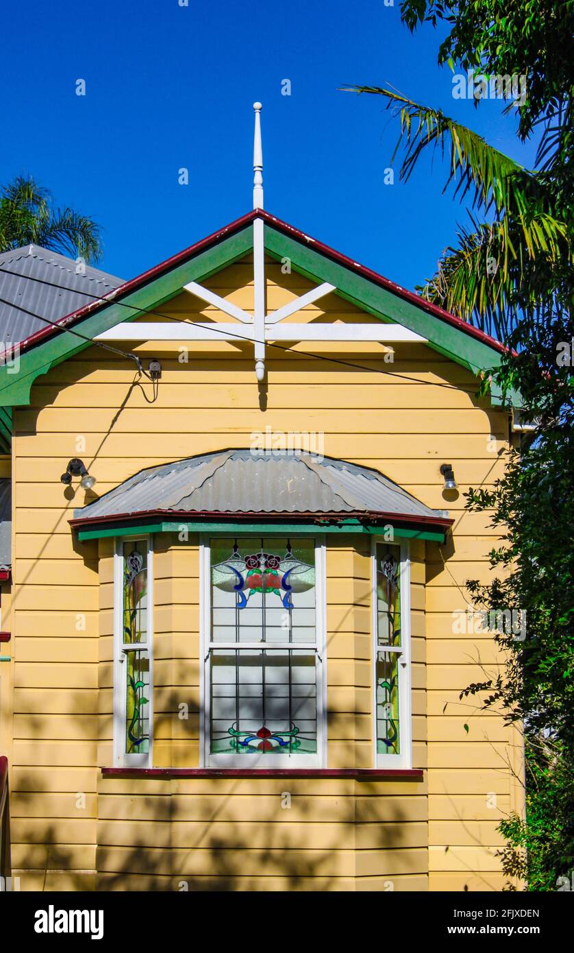 Baie vitrée sur jaune australien traditionnel Queenslander Maison avec toit en tôle et d'arbres tropicaux et intensément blule sky Banque D'Images