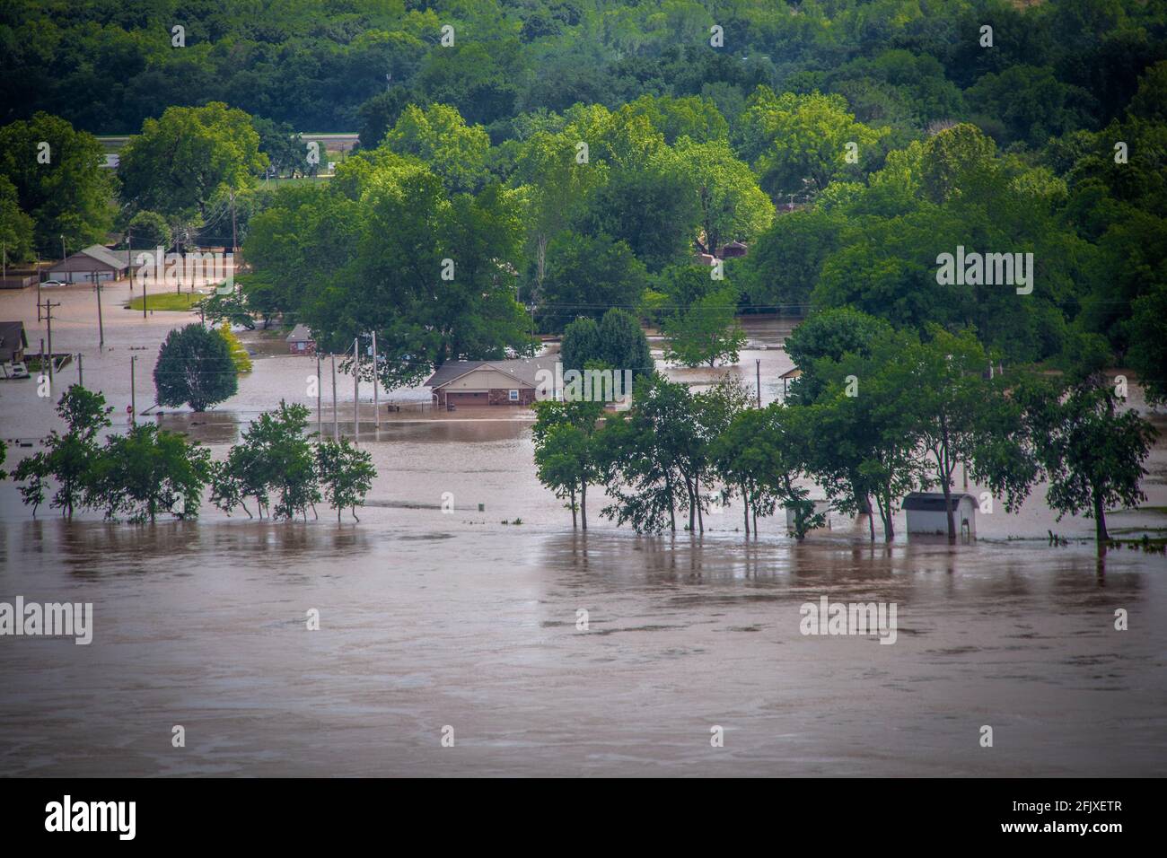 Maisons inondées et arbres dans la zone basse en face de colline verdoyante avec eaux brunes tourbillonnantes Banque D'Images