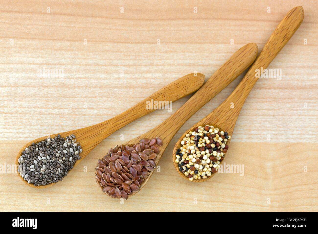 Graines de Chia séchées, graines de lin, graines de quinoa mélange de trois couleurs sur une cuillère en bois, fond de bois Banque D'Images