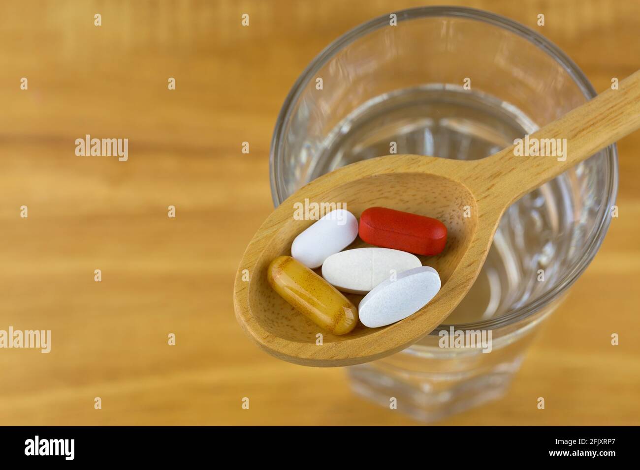 Compléments alimentaires en cuillère en bois, gelée royale en capsule de gel souple, comprimés pelliculés de multi vitamines et minéraux sur verre d'eau avec bois b Banque D'Images