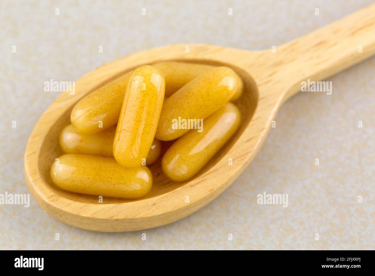 Gros plan concentré de gelée royale dans des capsules de gel souple dans une cuillère en bois, produits d'abeille de qualité supérieure utilisés comme supplément alimentaire Banque D'Images