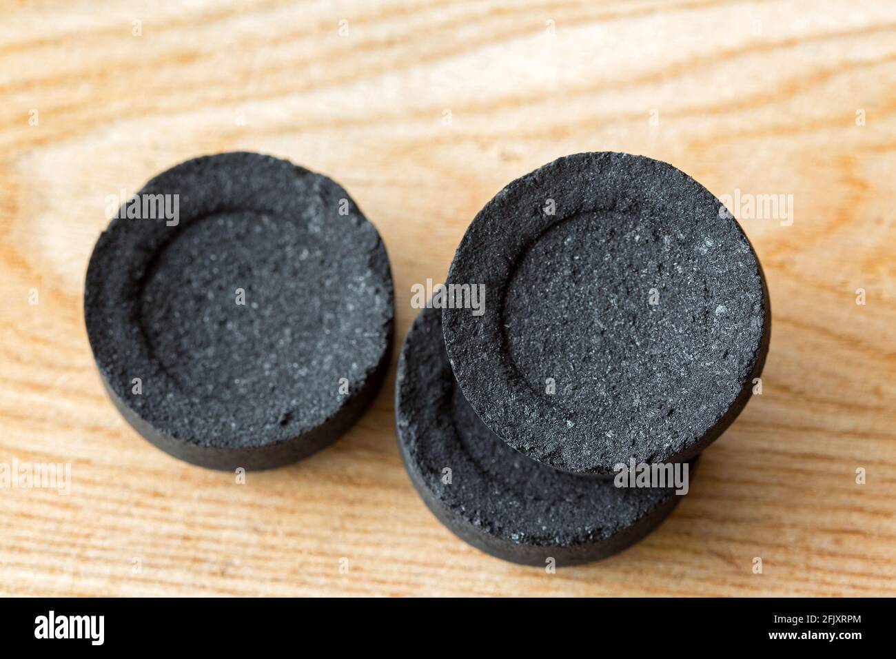 Disque rond noir de charbons arabes pour brûler l'encens aromatique, gomme de résine, sans additifs chimiques sur fond de bois Banque D'Images