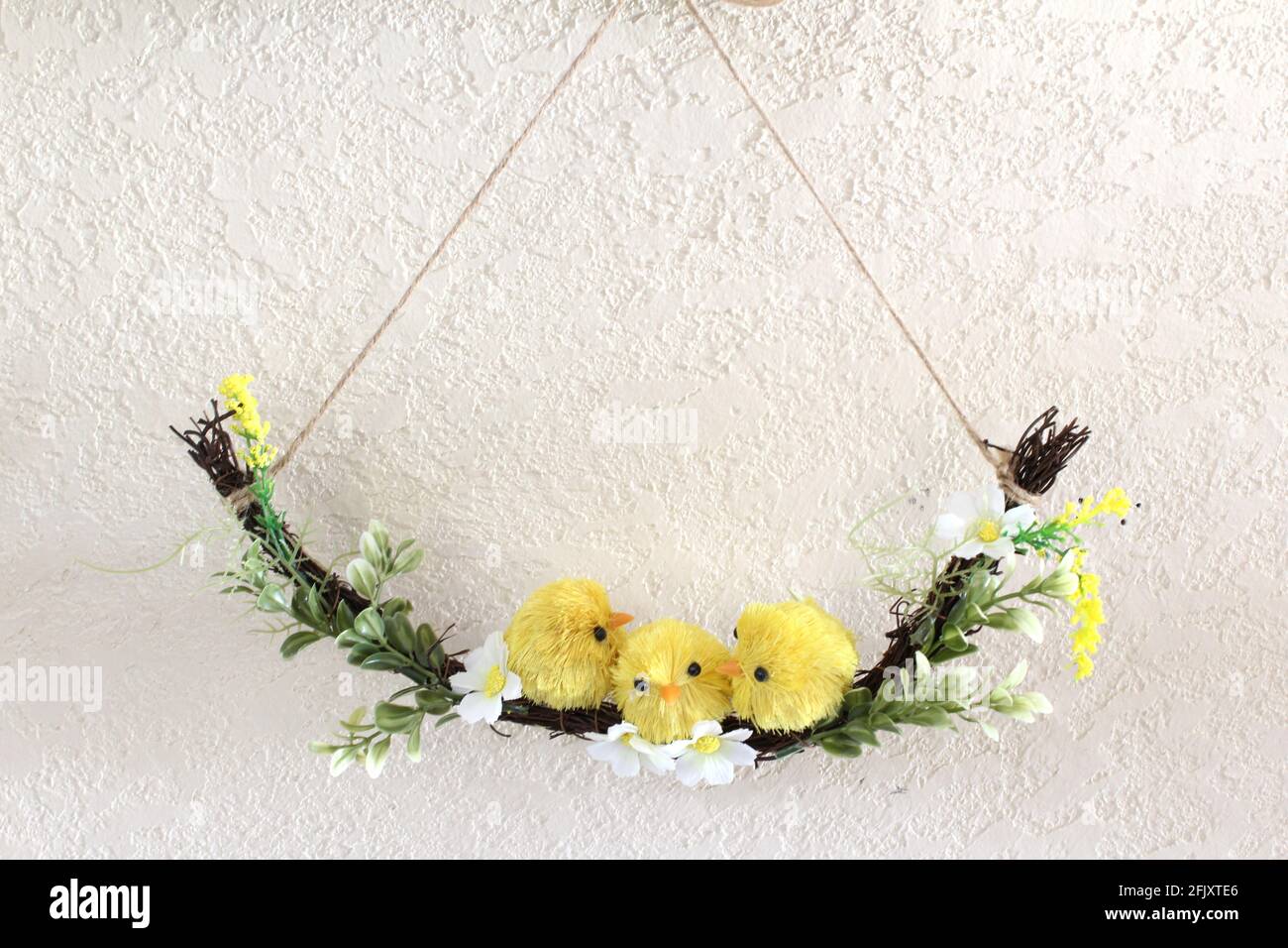Décoration de printemps, 3 petits poussins jaunes faux assis sur une branche balançoire faite de brindilles et de petites fleurs sur fond blanc, heure de Pâques. Copier l'espace Banque D'Images