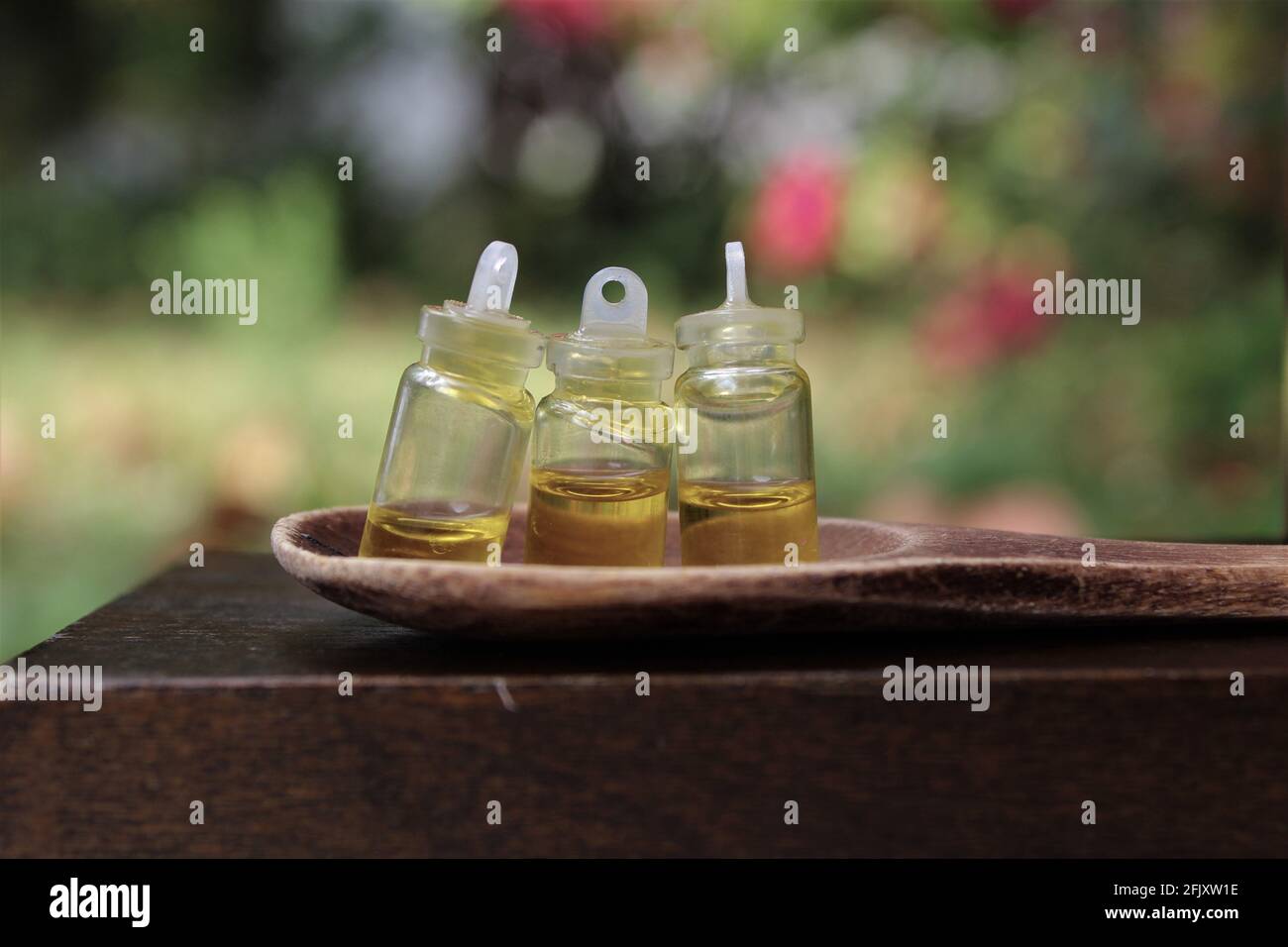 Bouteilles d'huile d'olive dans de minuscules bouteilles de teinture qui se trouvent dans un champ d'herbe sur une cuillère en bois, pour cuisiner avec un espace de copie Banque D'Images