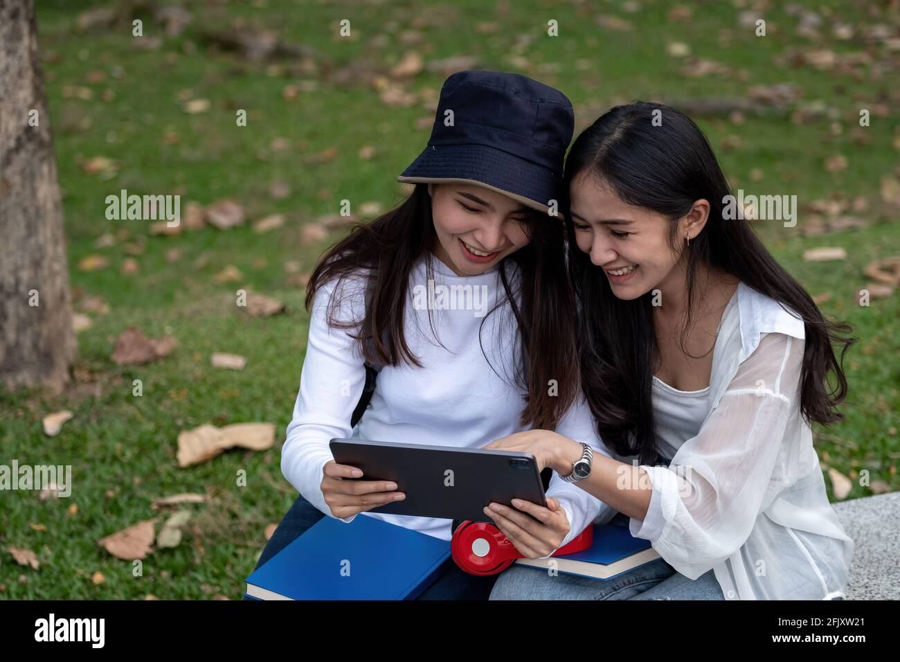 Deux étudiantes de l'université étudient en plein air, en utilisant une tablette numérique ensemble dans le parc de l'université Banque D'Images