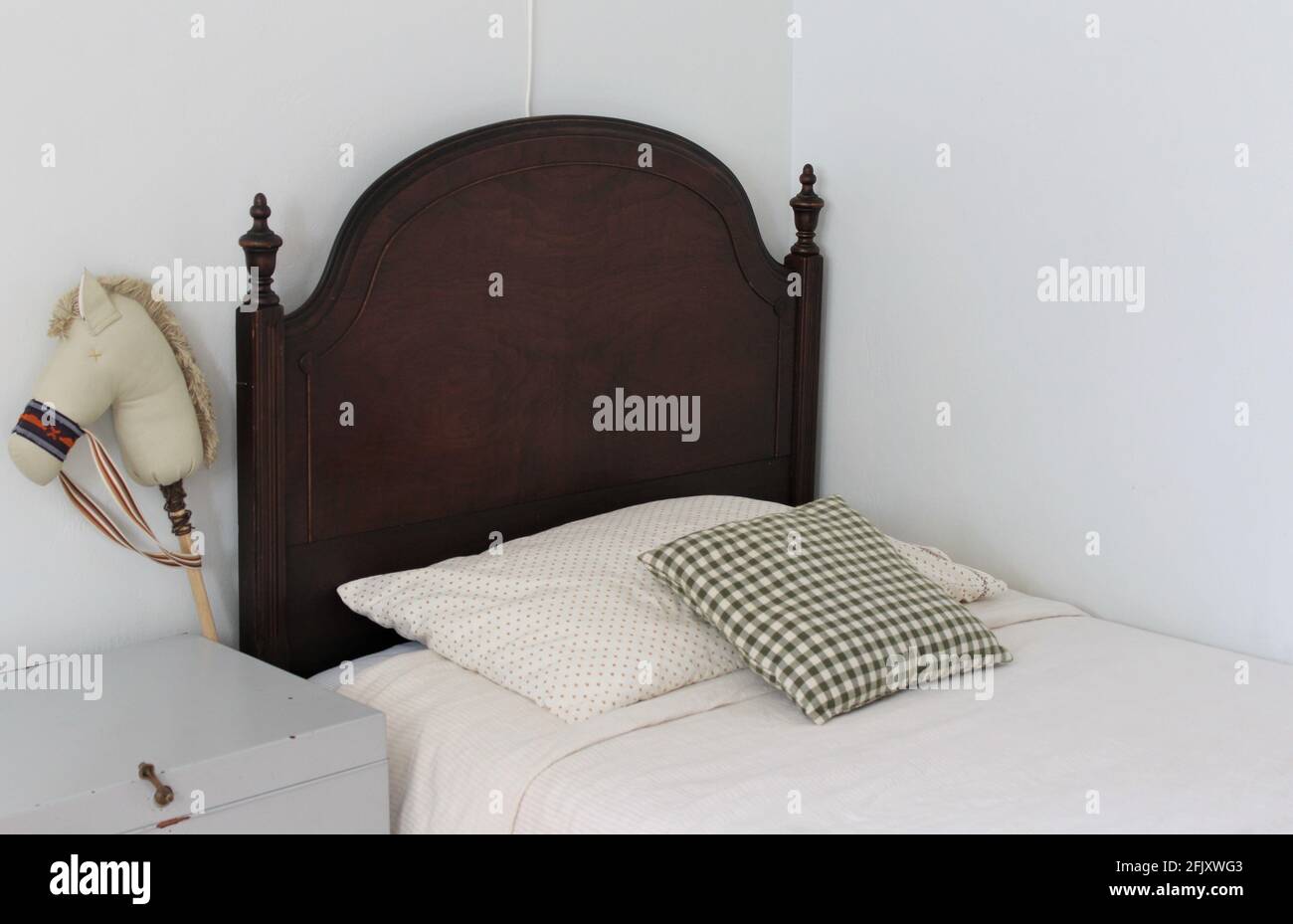 Chambre des enfants. Cadre de lit en bois avec petite lampe murale au-dessus du mur pour lire la nuit. Un cheval de jeu sur un stock est assis près du lit et le jouet vintage ch Banque D'Images