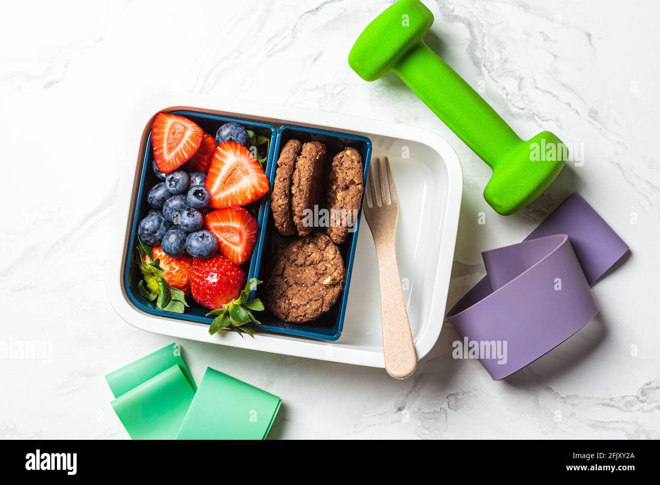 Des outils pour le sport et un panier repas santé sur fond de marbre blanc. Contenant avec fruits et biscuits à emporter. Banque D'Images