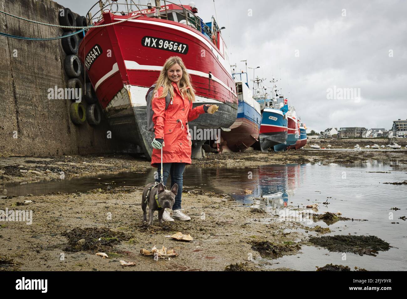 Femme blonde avec boudogue français dans le port de Roscoff à marée basse, chalutiers de pêche en arrière-plan Banque D'Images