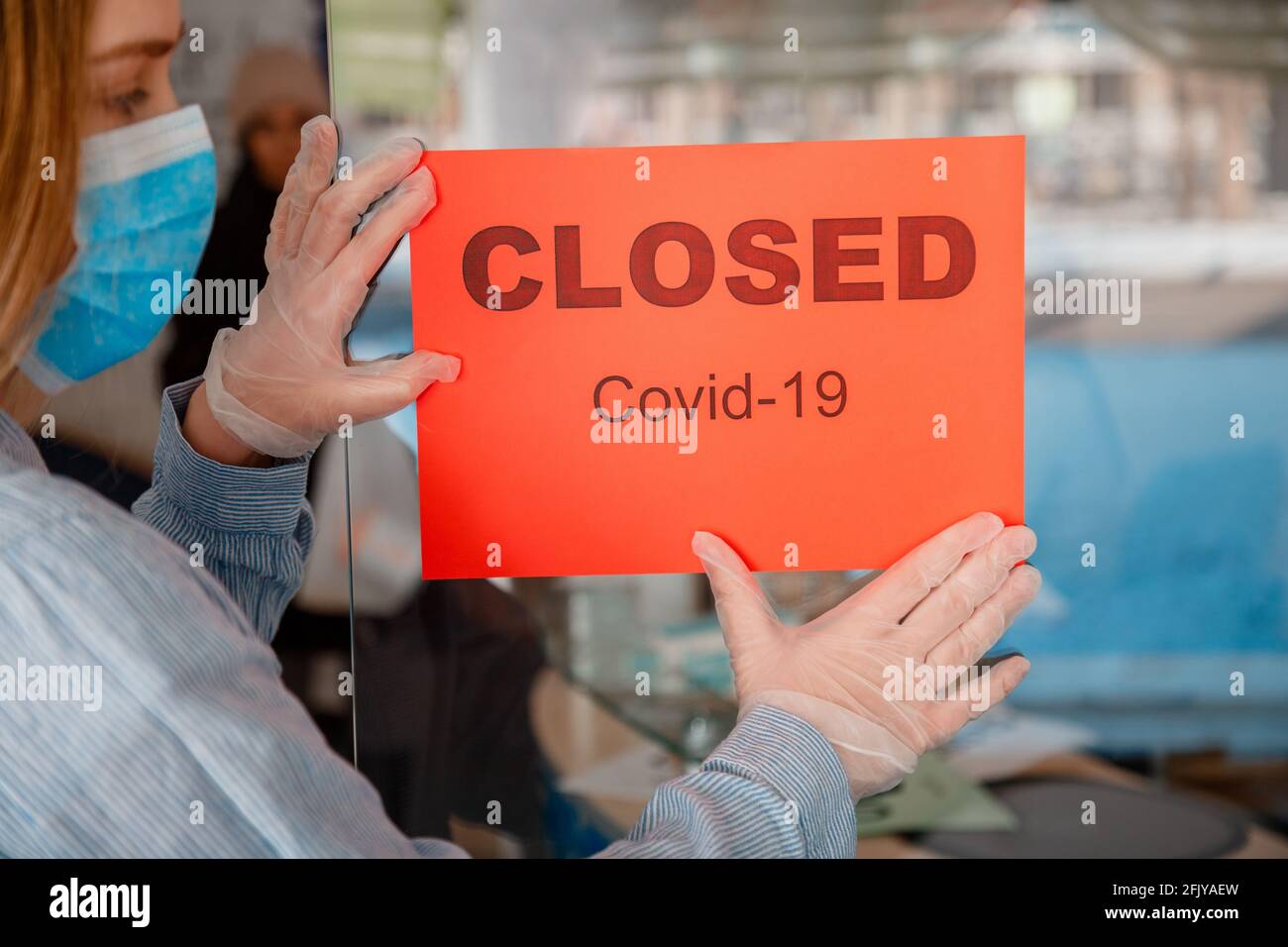 Le panneau rouge a fermé le verrou Covid 19 sur la porte d'entrée de l'atelier à titre de nouvel arrêt normal. Femme dans des gants de masque médical de protection porte une affiche fermée sur Banque D'Images