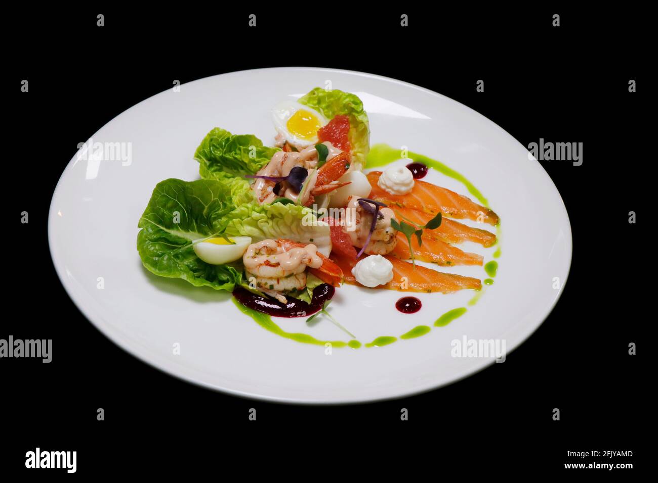 cocktail de crevettes et salade gravlax de saumon mariné avec petit bijou laitue et herbes dans une assiette blanche avec fond noir Banque D'Images