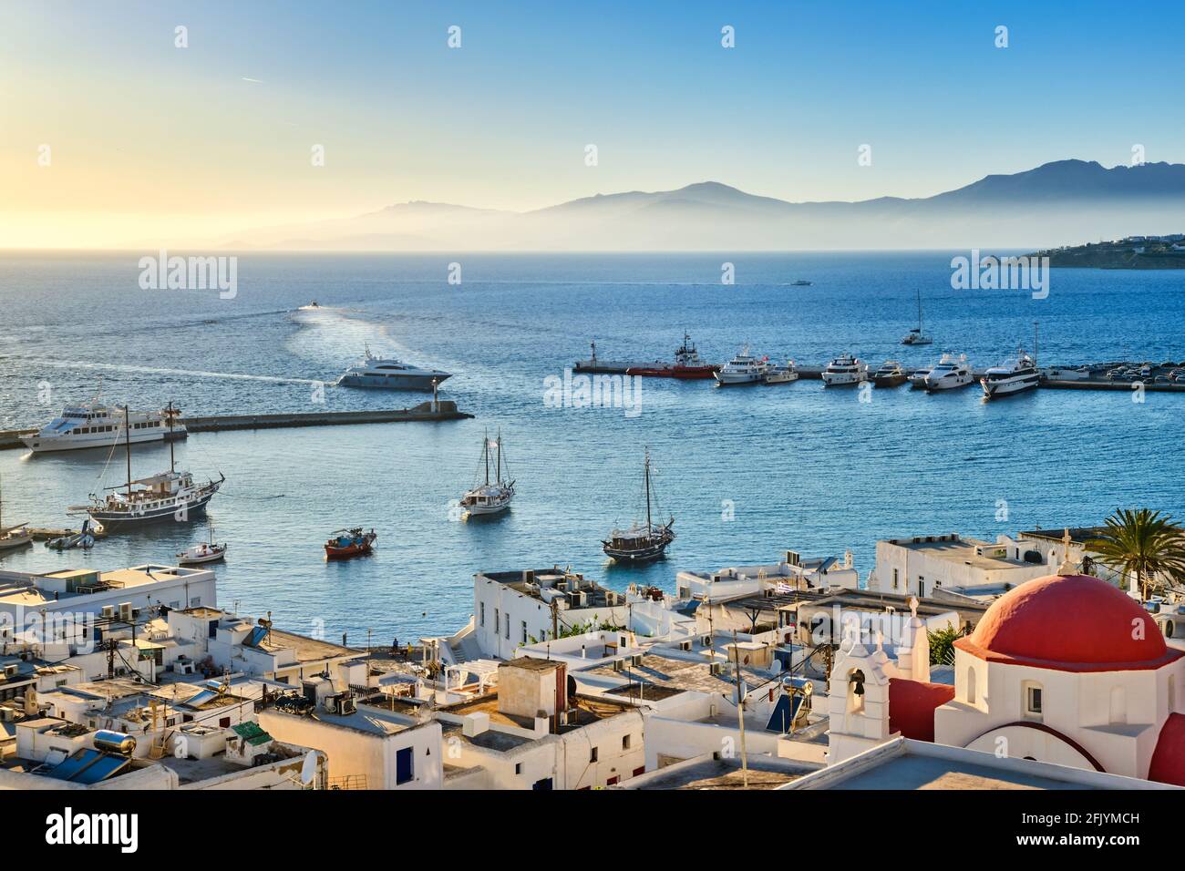 Belle vue sur Chora, Mykonos, Grèce au coucher du soleil. Port, baie, bateaux, yachts amarrés par la jetée. Célèbres maisons blanchies à la chaux, église blanche avec dôme rouge Banque D'Images