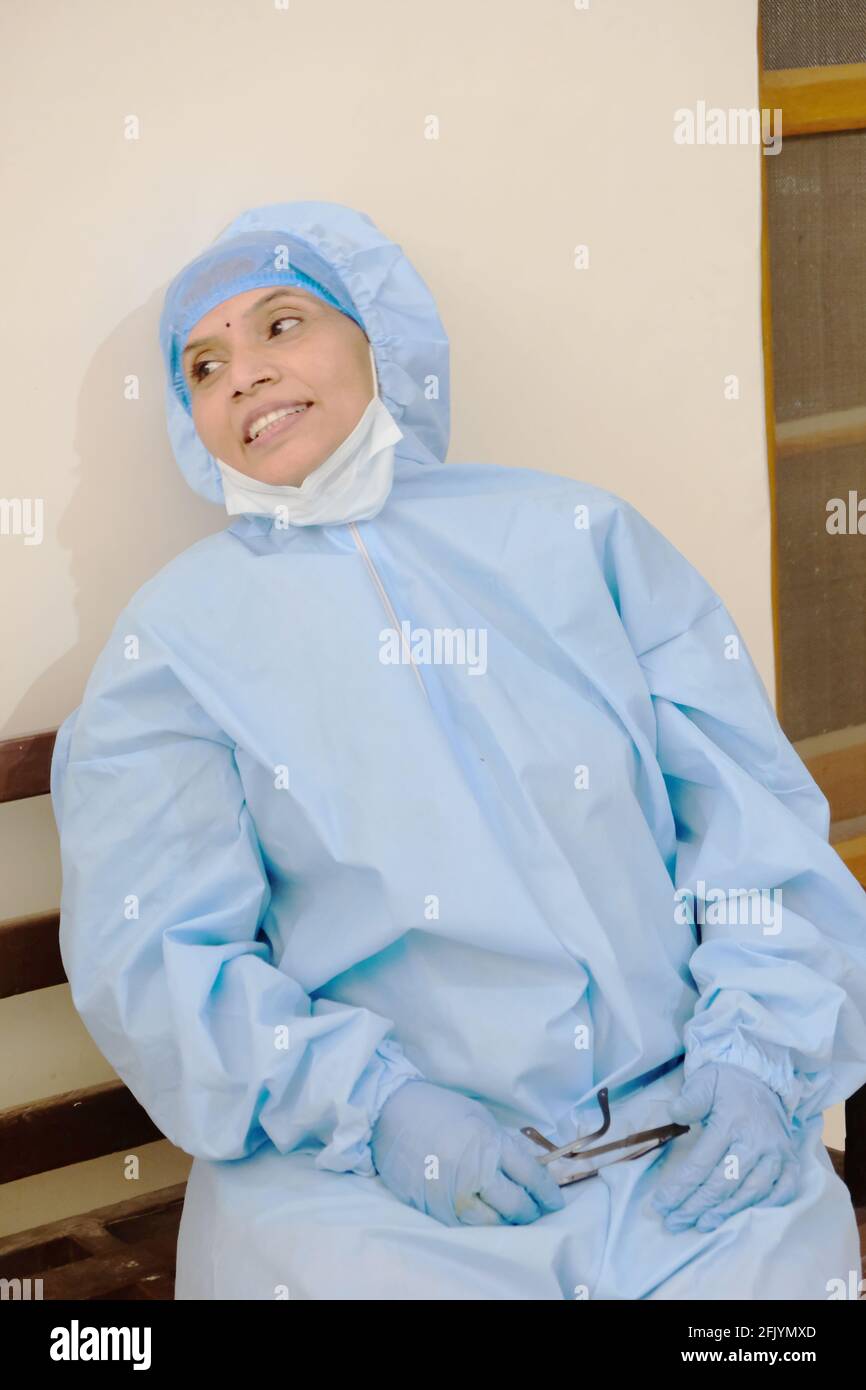 Tir vertical d'une infirmière indienne dans un costume de protection, des gants et un masque sur son menton Banque D'Images