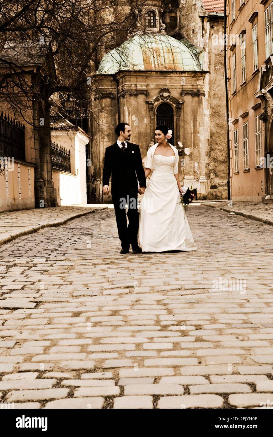 Magnifique couple de mariage (mariée et marié) marchant dans la rue en face de l'église historique et regardant l'un l'autre. Banque D'Images