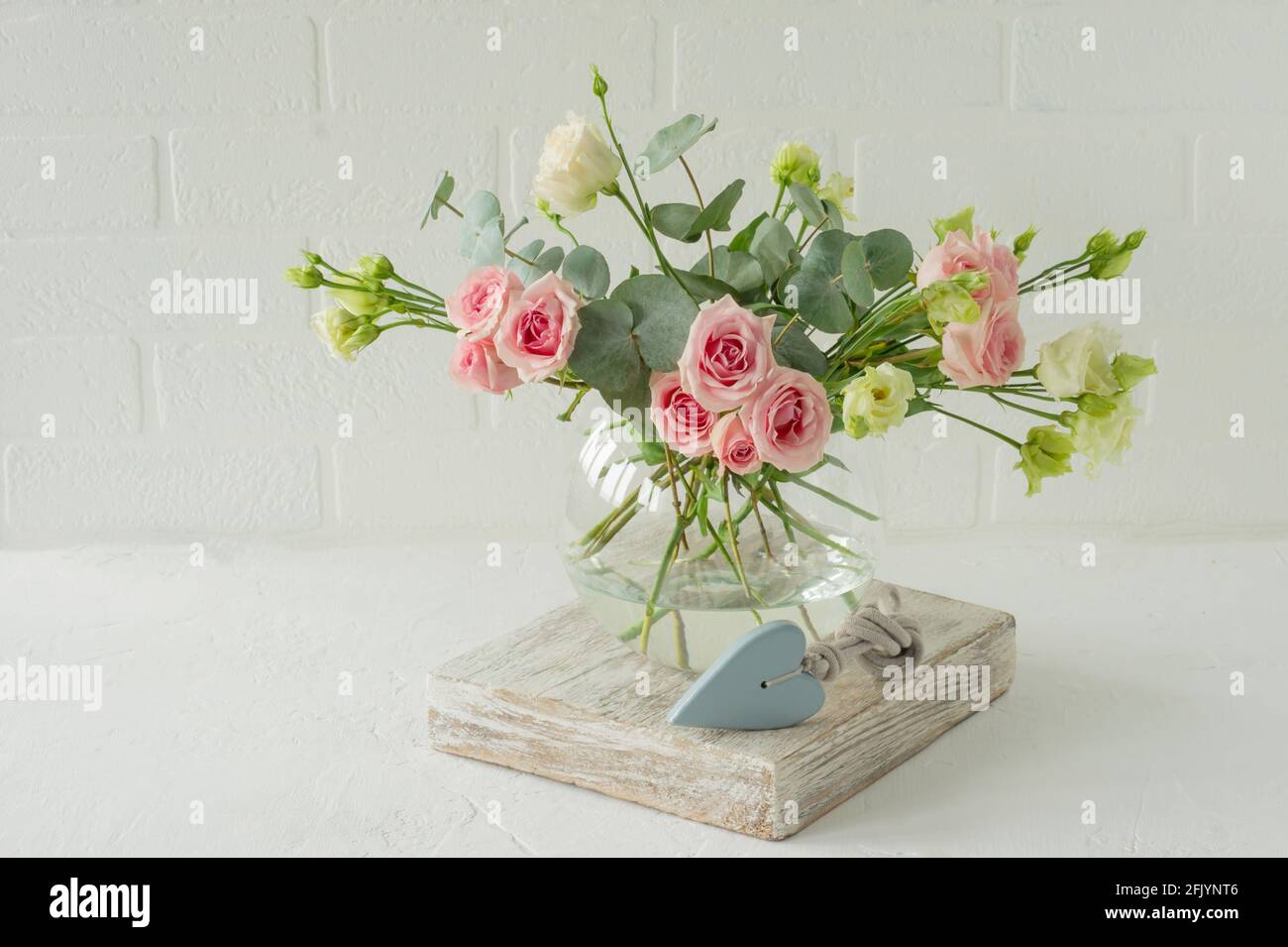 Bouquet de roses, d'euphorie et d'eucalyptus dans un vase en verre élégant sur une table. Composition des fleurs pour la décoration intérieure Banque D'Images