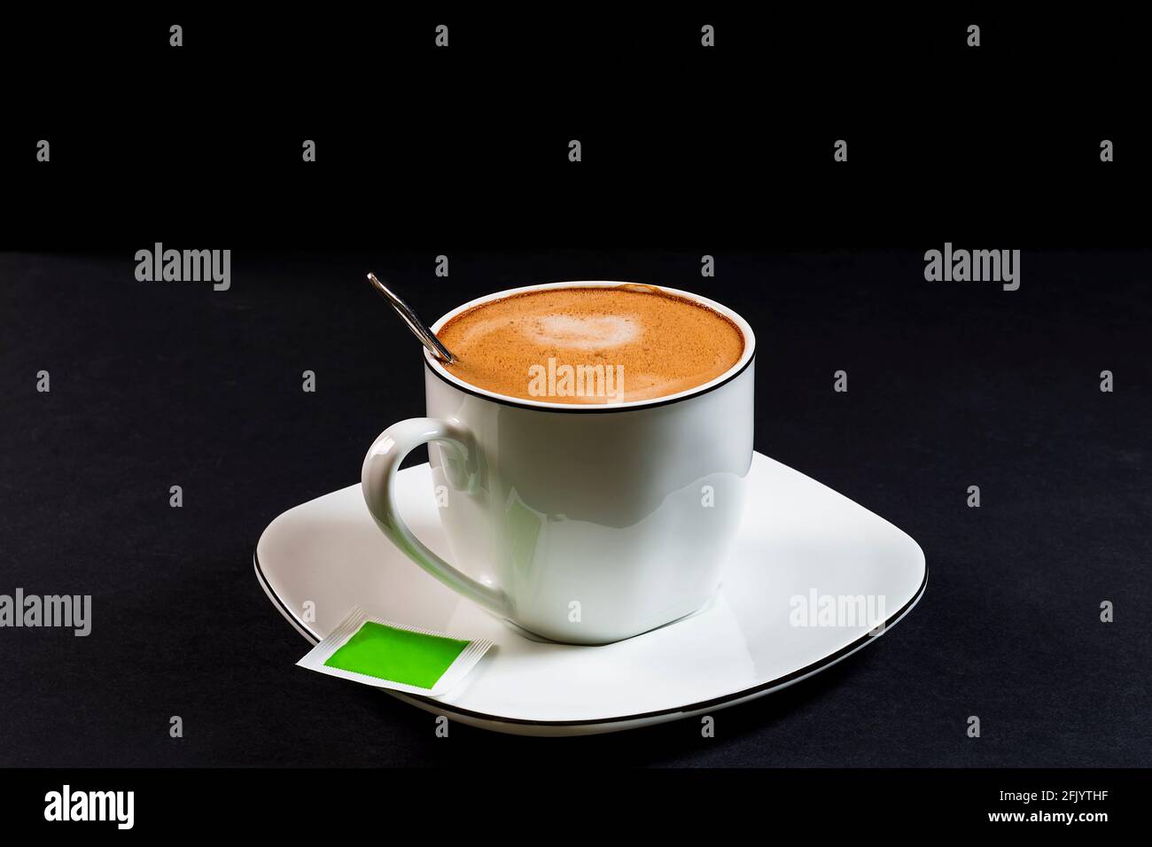 Café au lait dans une tasse en porcelaine décorative, une assiette, une cuillère et une enveloppe. C'est une photo horizontale prise sur un fond noir sous lumière artificielle i Banque D'Images