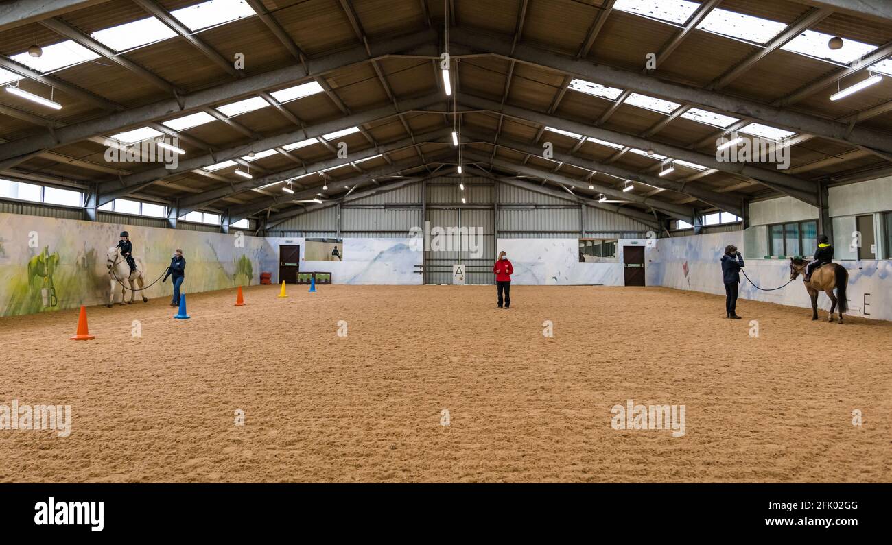 East Lothian, Écosse, Royaume-Uni, 27 avril 2021. Muirfield Riding Therapy rouvre: L'organisme de bienfaisance accueille ses premiers jeunes pour leur séance de thérapie avec des restrictions de verrouillage assouplies. En raison de restrictions continues, seuls les clients plus mobiles peuvent être pris en charge pour le moment. Photo : Nathan et Fin, tous deux âgés de 10 ans et amis de l'école primaire de yester sur leurs chevaux de thérapie instruits par l'entraîneur Shirley Duff dans l'arène Banque D'Images