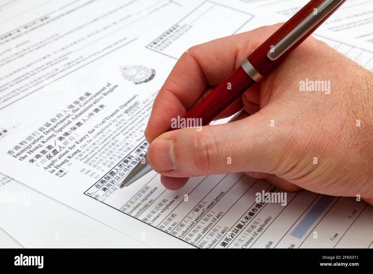 Un homme tenant un stylo à bille pour remplir un formulaire de demande de visa pour Hong Kong. Banque D'Images